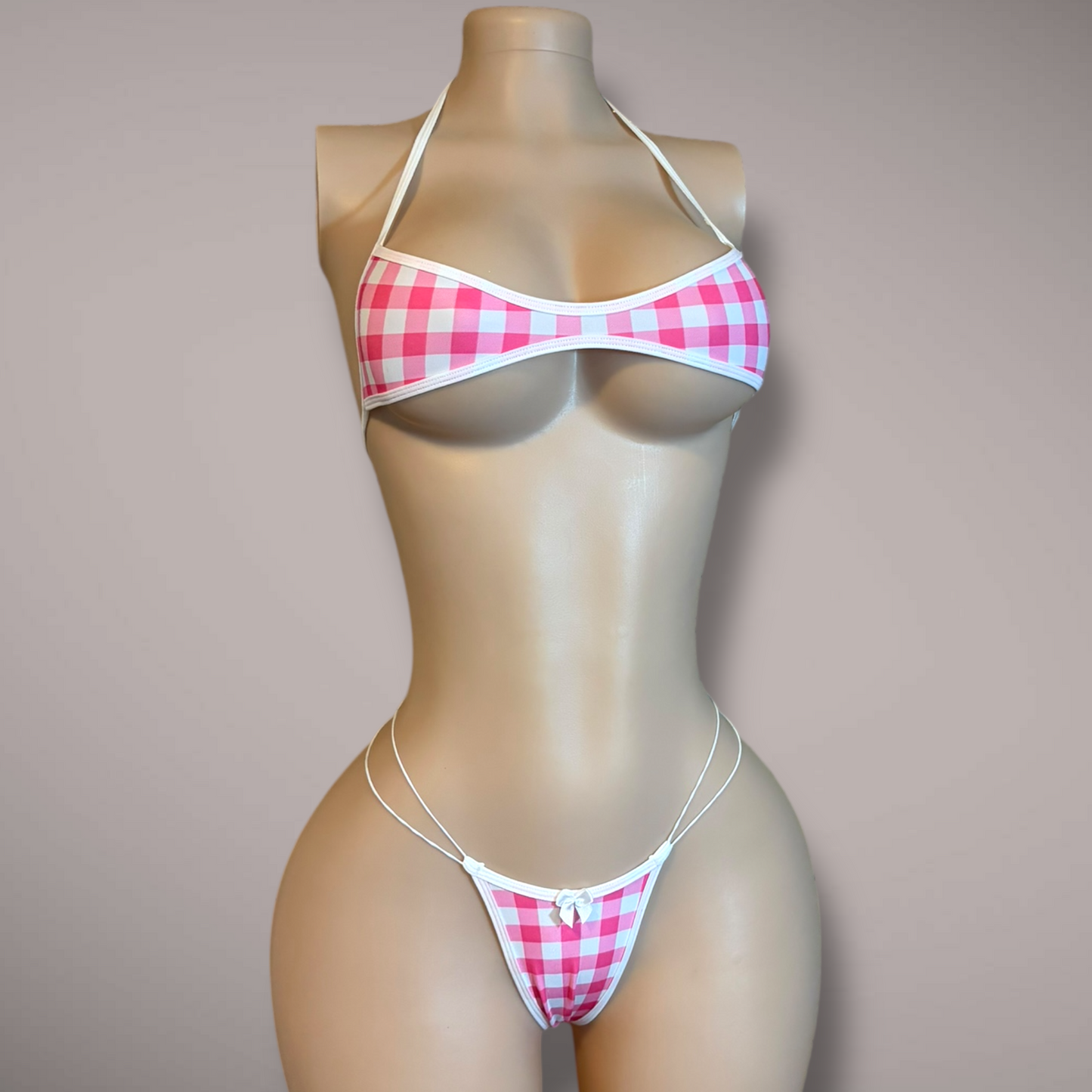Front view of pink gingham bikini set on mannequin with white trim, halter top, bow detail, and ultra minimal thong bottoms.
