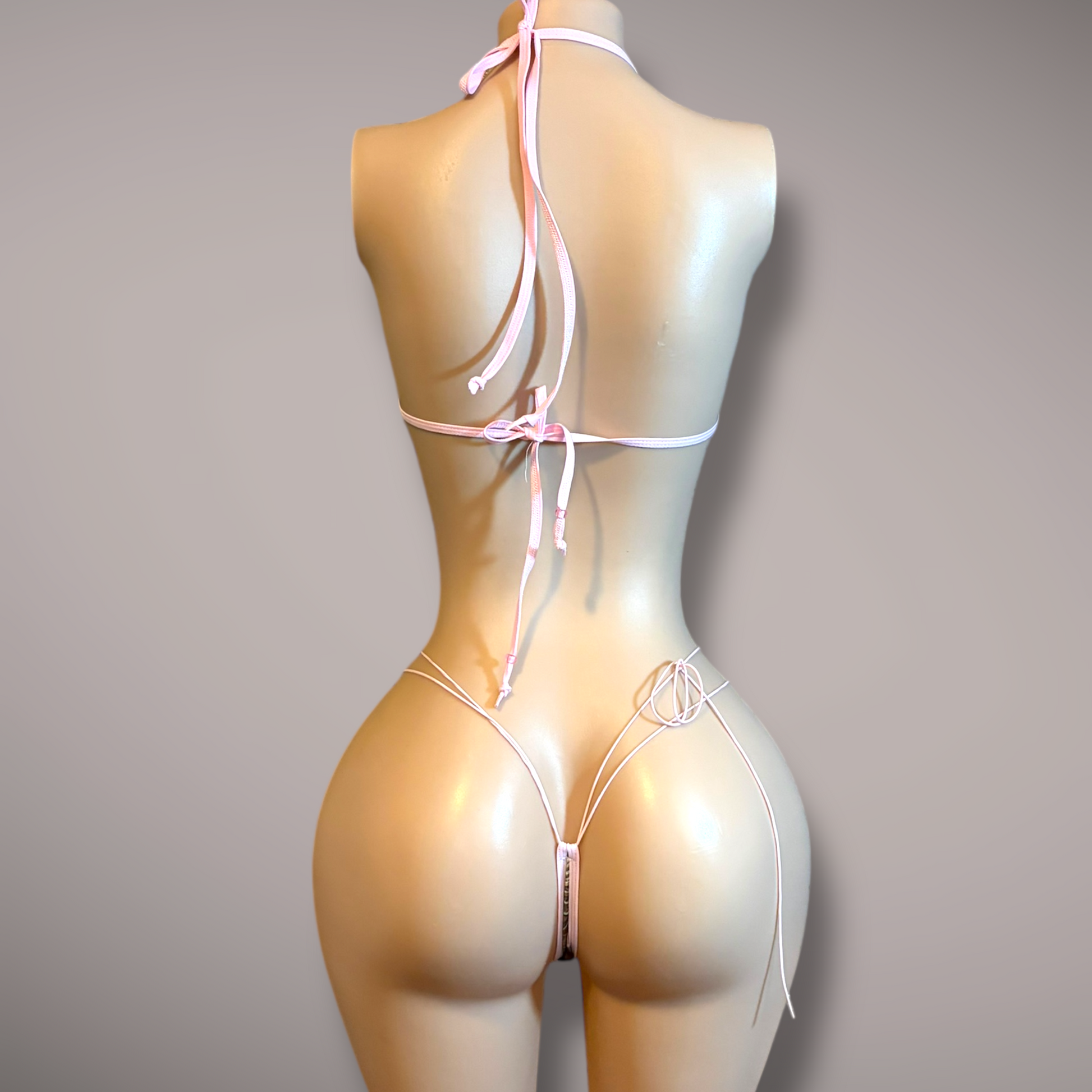 Back view of a camo micro bikini with pink ties on a mannequin, showing adjustable neck, back, and side ties with a minimal thong design.