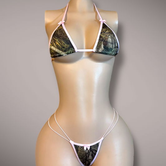 Front view of a camo print micro bikini with pink trim and bow details on a mannequin, featuring a triangle top and strappy thong bottom.