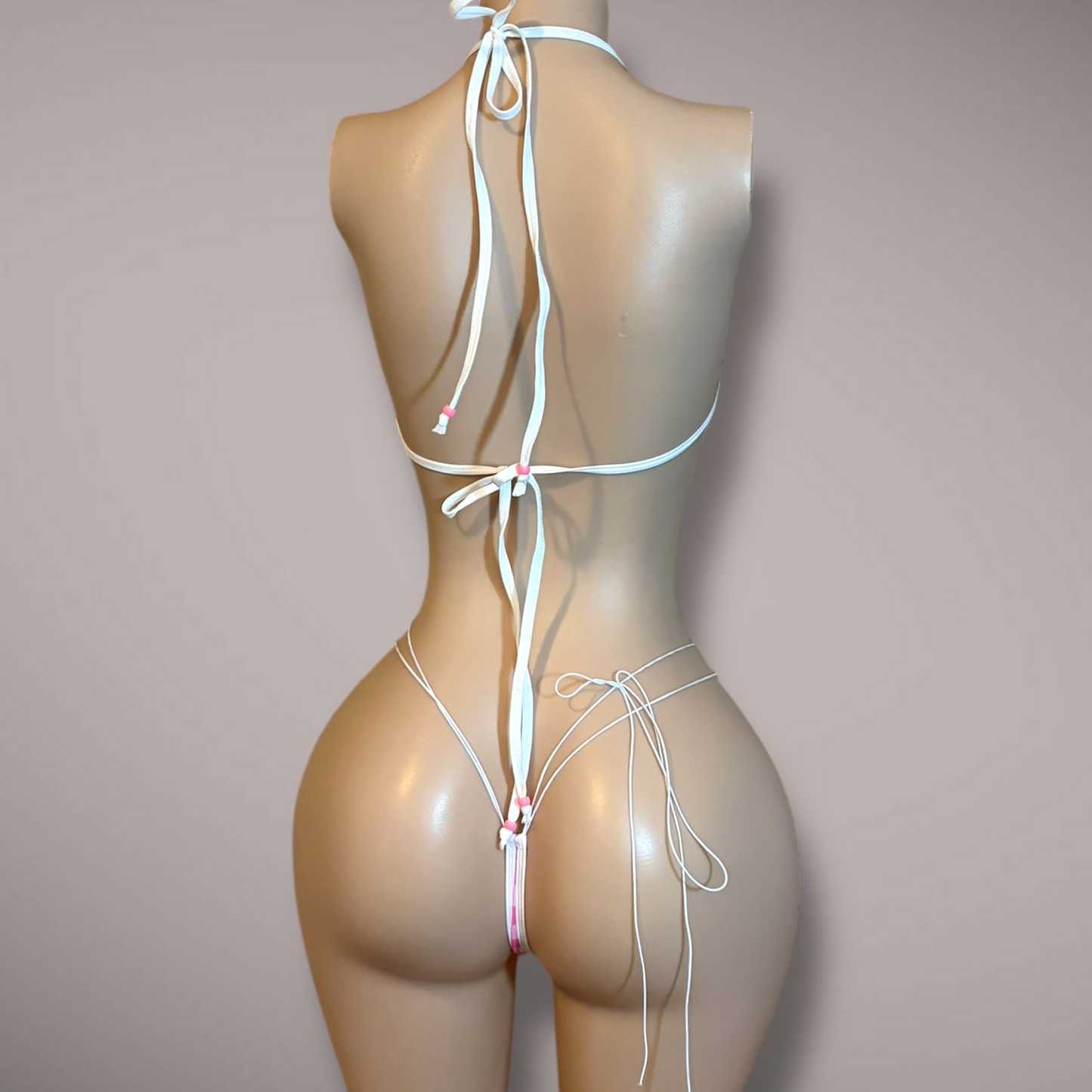 Back view of pink gingham bikini set on mannequin showing adjustable ties, halter straps, and minimal thong with string back detail.